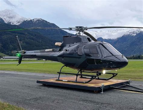 A Helicopter Sitting On Top Of An Airport Tarmac With Mountains In The